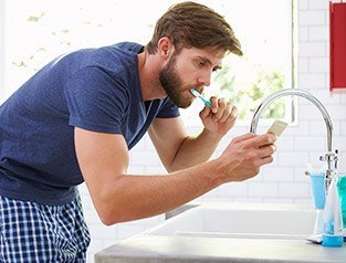 man brushing teeth while on cellphone