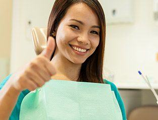 Woman gives thumbs up while sitting in dental chair