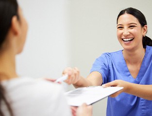 a front desk worker handing a patient forms on a clipboard