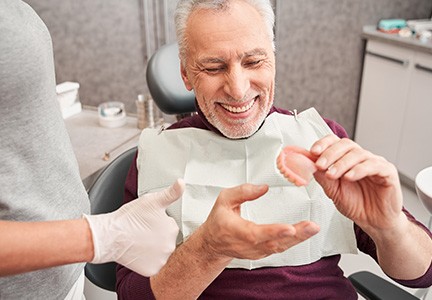Man smiling and holding dentures in Greenfield