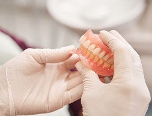 Closeup of white-gloved hands holding complete set of dentures
