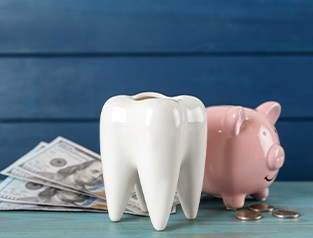 Piggy bank next to large model tooth and dollar bills