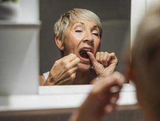 Woman flossing her teeth in bathroom mirror