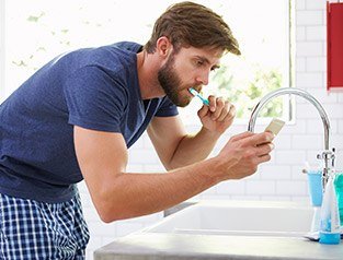 man brushing teeth while on cellphone