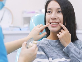 Paciente señalándose los dientes mientras el dentista se prepara para la consulta.