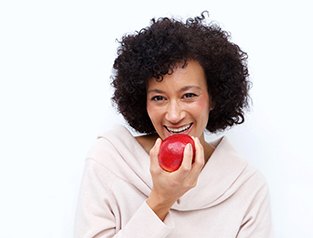 Woman with dental implants in Greenfield eating an apple