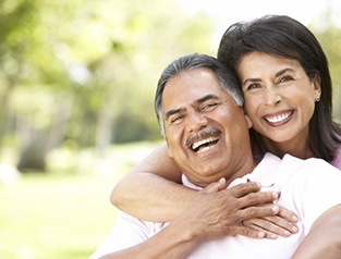 Healthy couple with dental implants in Greenfield laughing outside