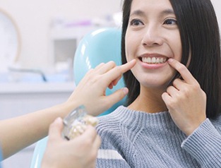 A woman pointing at her smile with a dentist