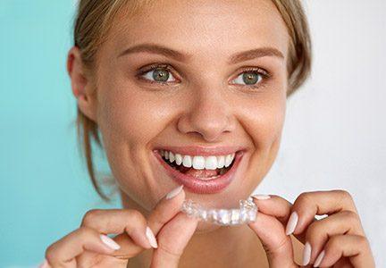 Smiling, healthy woman holding Invisalign in Greenfield