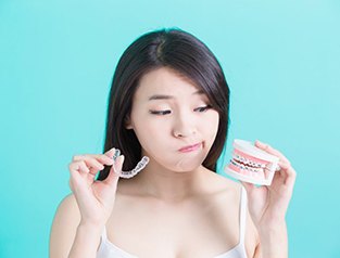 Wondering woman holding model teeth with braces and Invisalign