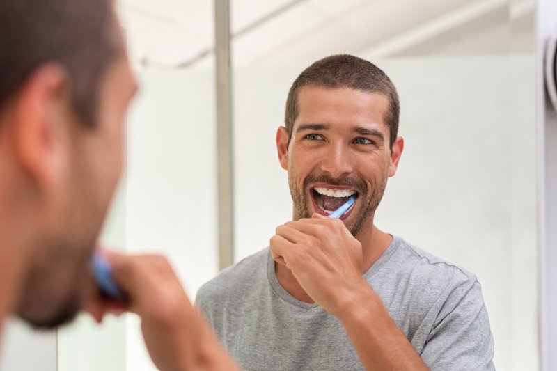 man brushing teeth in bathroom mirror
