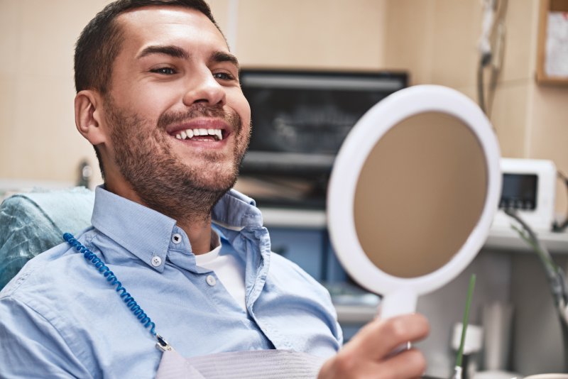 A handsome man admiring his teeth in a hand mirror